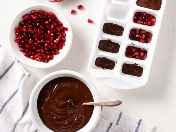 Bowl of chocolate and pomegranate seeds next to ice cube tray