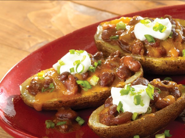 Chili potato skins topped with melted cheddar cheese, beans, sour cream and green onions on a red plate
