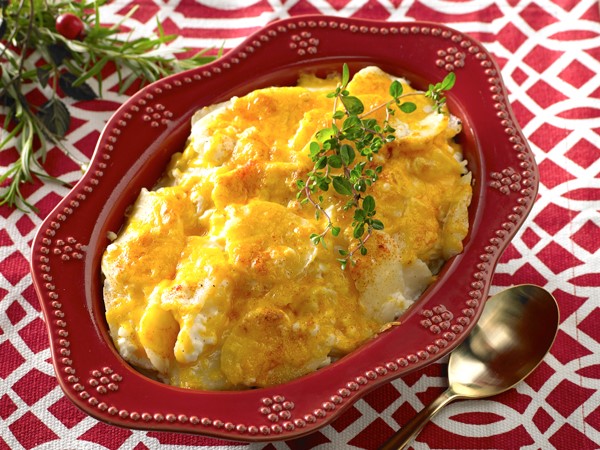 Red dish filled with potato casserole and topped with cheddar cheese and paprika 