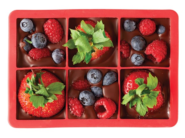 Red ice cube tray filled with melted chocolate and strawberries, blueberries and raspberries