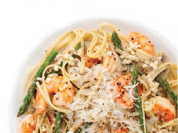 White bowl filled with linguine noodles, topped with asparagus, shrimp and parmesan