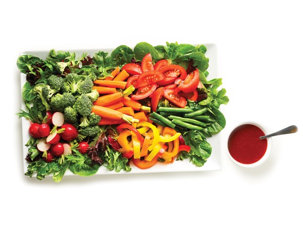 Platter of greens topped with radishes, broccoli, carrots, peppers, tomatoes and peas and served with a side of raspberry vinaigrette