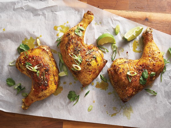 Three chicken leg quarters rubbed in seasoning and garnished with green onion, cilantro and lime