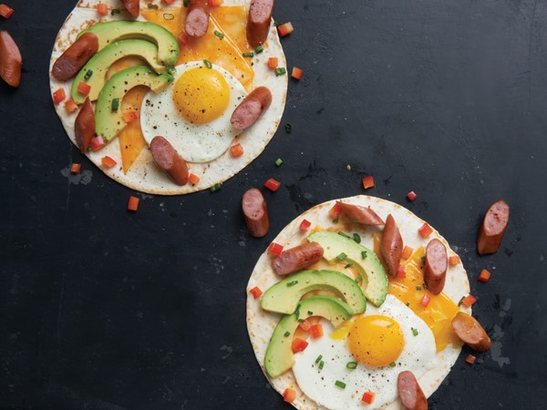 Tortilla topped with cheese, egg, avocado, sausage, onion and tomato