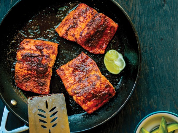 Three salmon fillets in skillet with wedge of lime