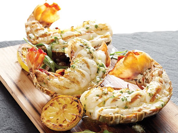 Planked lobster tails with grilled lemons on wooden slab