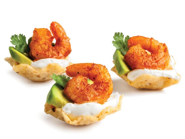 Scoop tortilla shells filled with sour cream, avocado slice, cilantro and seasoned shrimp