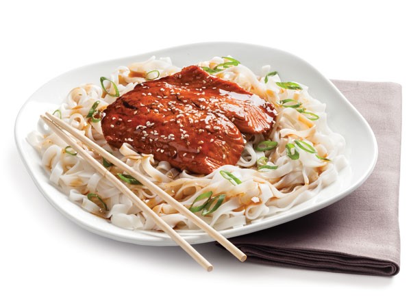 Plate of Asian-glazed salmon fillets over cooked rice noodles and green onion with wooden chopsticks