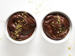 Two small white bowls filled with chocolate avocado pudding, garnished with crushed pistachios