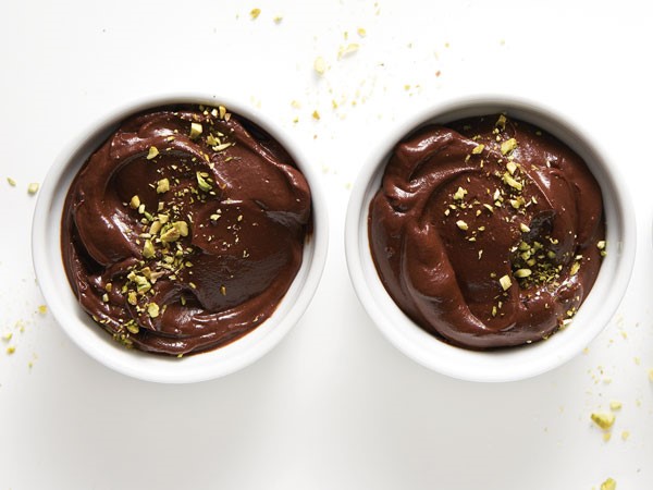 Two small white bowls filled with chocolate avocado pudding, garnished with crushed pistachios