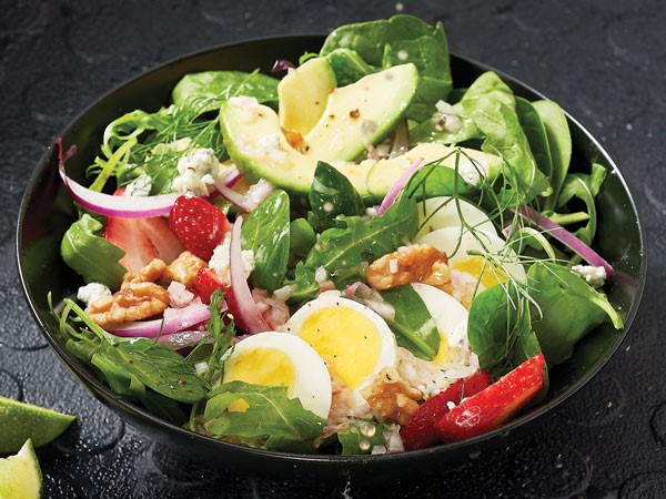 Bowl of greens mixed with strawberries, avocado, hard-boiled eggs, onion and pecans