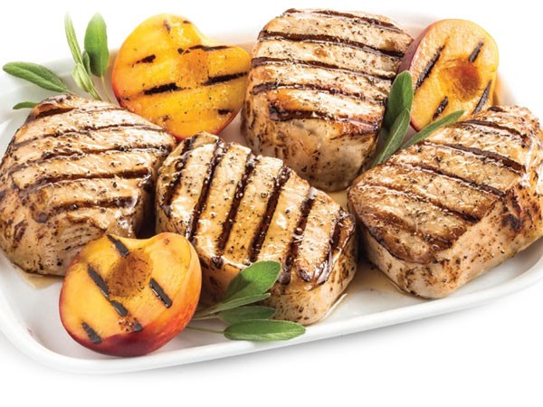 Grilled honey glazed pork chops garnished with sage and grilled peaches