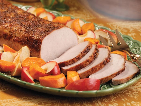 Platter of slice pork roast surrounded by baked apple slices and sweet potatoes