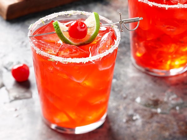 Sugar-rimmed glass filled with cherry-lime margarita, garnished with lime slice and maraschino cherry