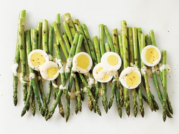 Pile of grilled asparagus topped with cheese sauce, egg slices and freshly ground pepper