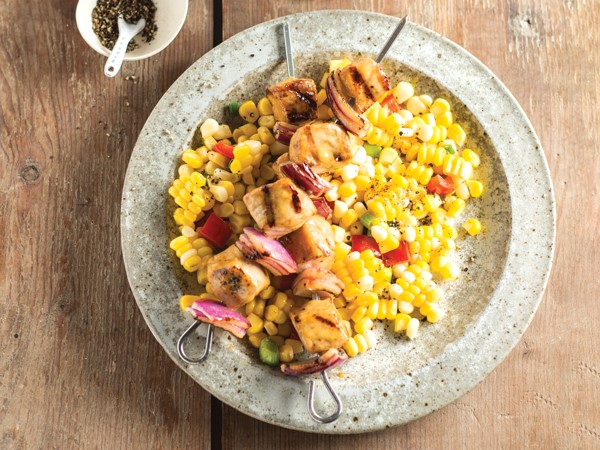 Bowl of sweet corn medley topped with honey mustard pork skewers