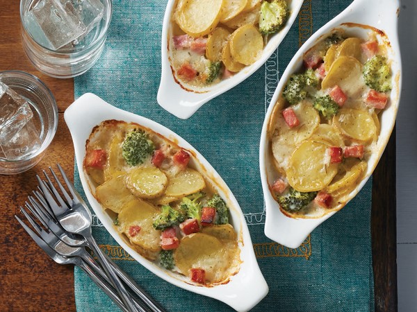 Dish of scalloped potatoes garnished with broccoli and ham cubes