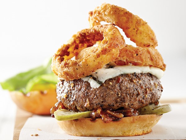 Bun topped with pickles, burger, blue cheese slice, and fried onion rings