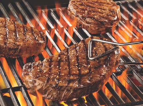 Coca cola-marinated rib eye steaks over a fire grill