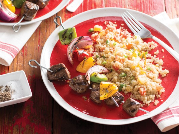 Quinoa salad next to grilled steak and vegetable kabobs