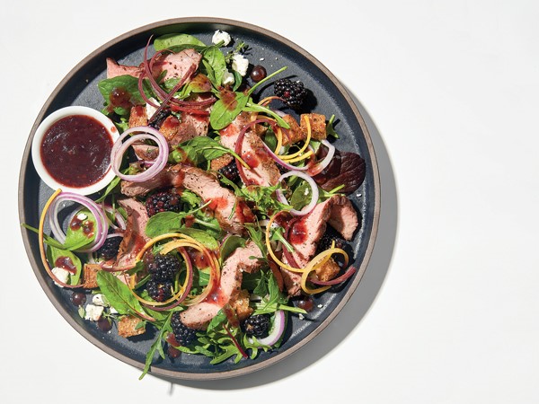 Salad topped with blackberries, greens, steak, and onions