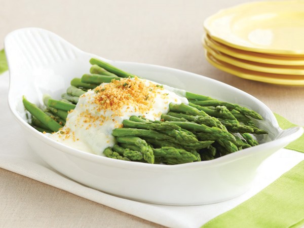 White dish of steamed asparagus topped with cream sauce and breadcrumbs