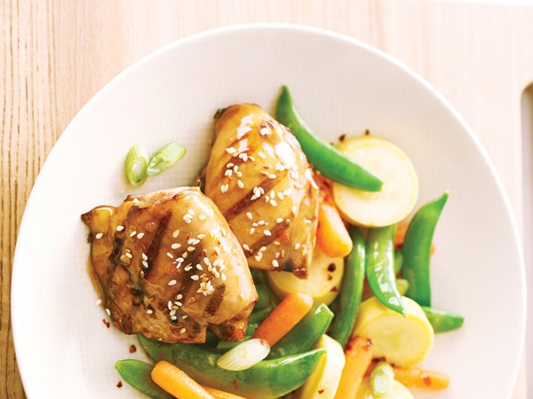 Sesame topped grilled chicken thighs with vegetables on white plate