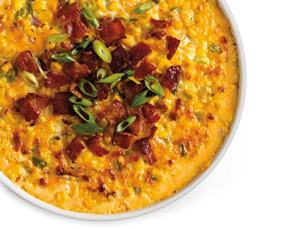 Dish filled with cheesy corn casserole and topped with crumbled bacon bits and chopped green onions