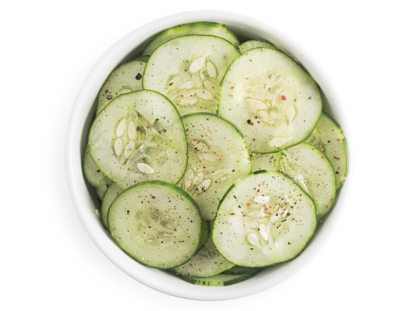 Bowl of cucumber salad topped with freshly ground black pepper
