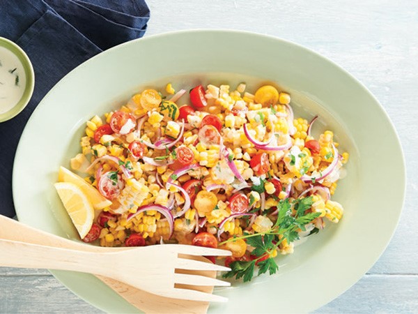 Bowl filled with creamy corn salad with wooden serving utensils
