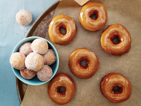 Blue bowl of coffee doughnut holes covered in coffee sugar next to coffee doughnuts topped with coffee icing on parchment paper