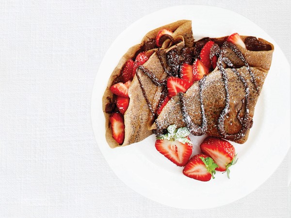 Crepe filled with hazelnut spread and topped with strawberries, chocolate-hazelnut drizzle and powdered sugar