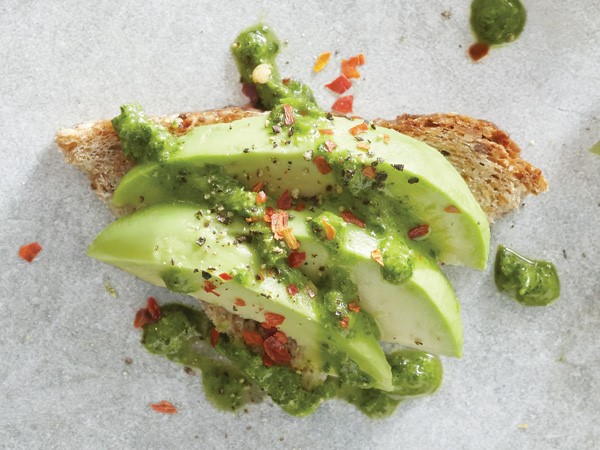 Whole-grain bread slice topped with avocado, arugula mixture and red pepper flakes