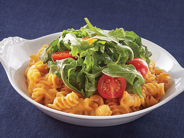 Mac and cheese topped with tomatoes and fresh arugula