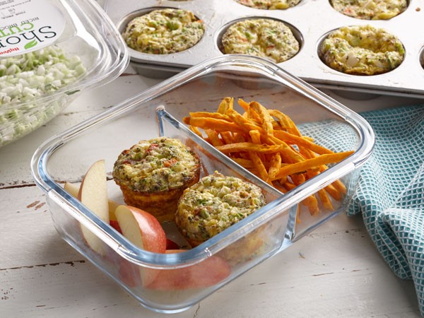 Plastic container with two baked egg muffins, apple slices and sweet potato fries