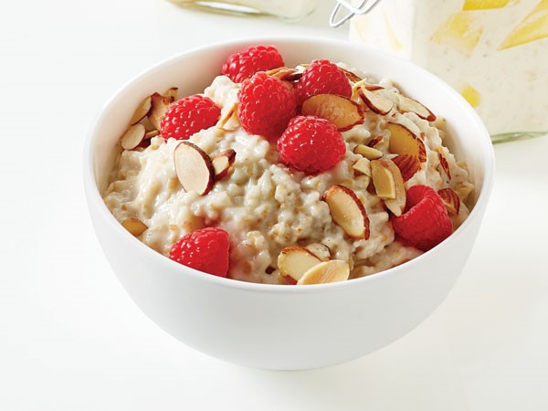 Oatmeal in white bowl topped with sliced almonds and raspberries