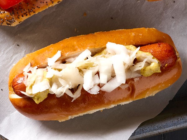 Hot dog in bun topped with onions, sauerkraut, and spicy mustard