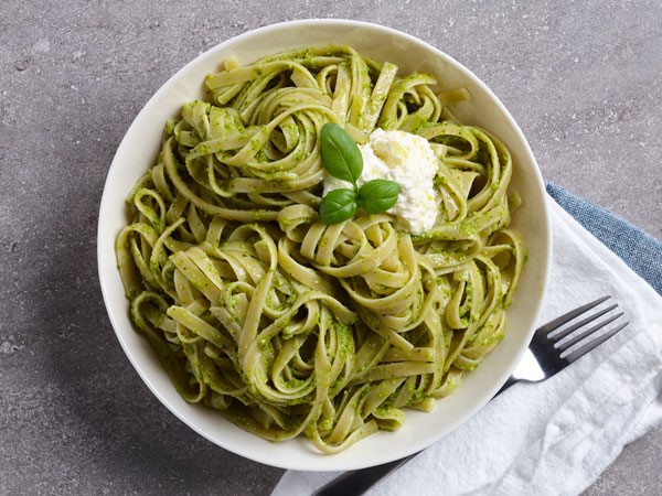 Linguini noodles covered with pesto with a dollop of ricotta and sprig of fresh basil