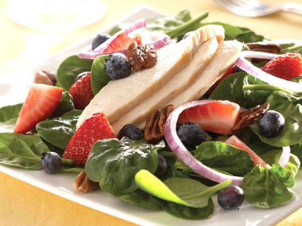 Plate of spinach topped with strawberries, blueberries, chicken slices, red onion, pecans and vinaigrette