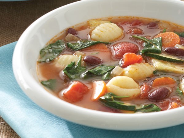 Spinach gnocchi soup in white bowl with blue napkin