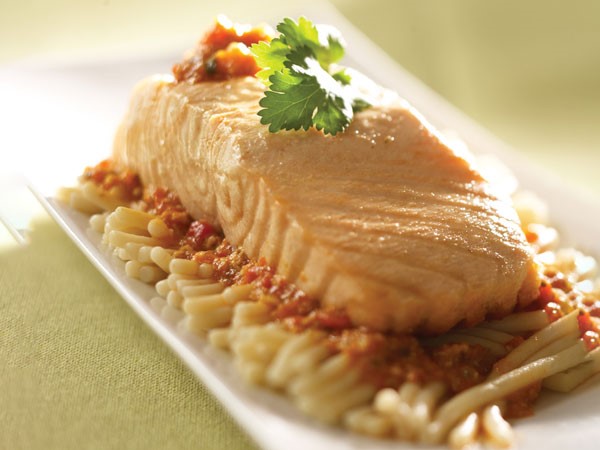 Plate of baked salmon over pasta covered in red pepper sauce