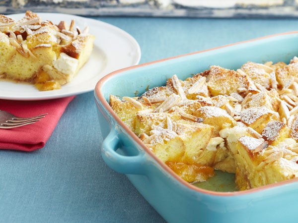 Peaches and cream French toast in teal casserole dish with slice on white plate