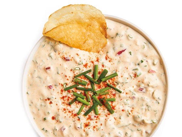 Party dip in white bowl topped with chopped chives and kettle chip