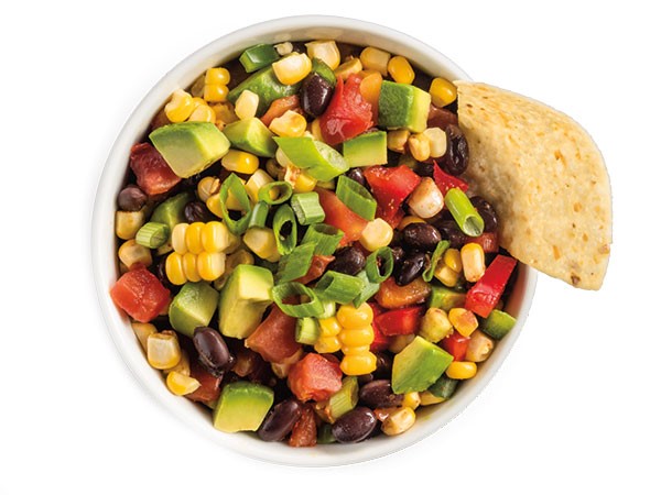 Chunky avocado salsa with corn, black beans, and tomatoes with chip.
