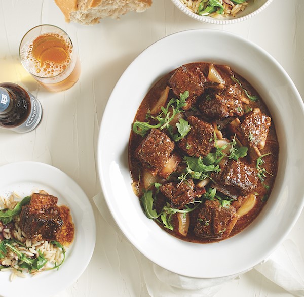 Bowl of beer-braised short ribs with onions and arugula leaves