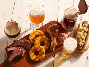 White wooden background with beer, brats, grilled pineapple, chicken, and ribs