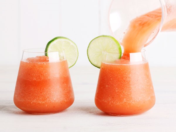 Two glasses of strawberry frozen slushy, garnished with lime slices