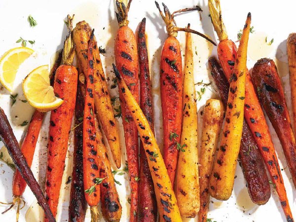 Grilled carrots covered in honey-lemon sauce and garnished with thyme and lemon wedges