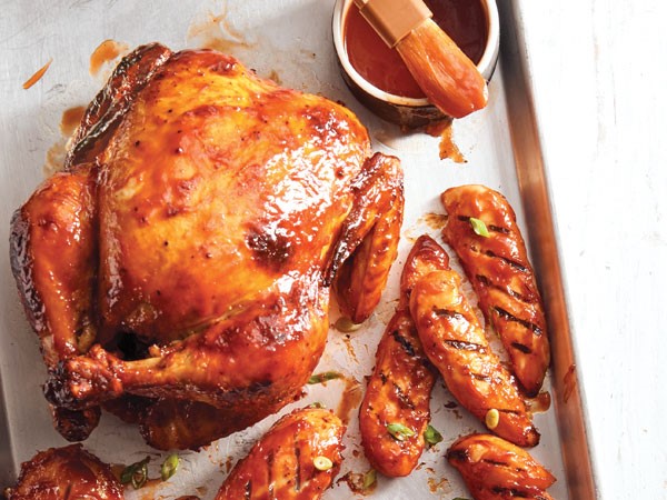 Chicken tender and whole chicken covered in homemade bbq sauce on tray with side of sauce and brush