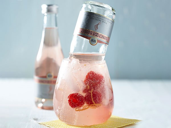 Glass filled with cherry-berry sangria, raspberries and orange zest with a Barefoot Bubbly floater